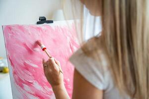cerca arriba ver de joven mujer artista con paleta y cepillo pintura resumen rosado imagen en lona a hogar. espalda vista. Arte y creatividad concepto foto