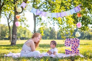 Cheerful mother and daughter having fun on child birthday on blanket with paper decorations in the park photo