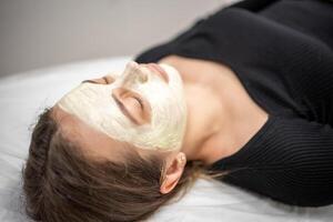 Beautiful happy woman in the spa making face mask treatment. Beauty industry concept. photo