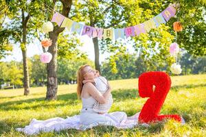 Cheerful mother and daughter having fun on child birthday on blanket with paper decorations in the park photo