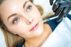 Close-up of woman face and hand in surgical glove holding syringe near her lips, ready to receive beauty treatment. Injection cosmetology, lips augmentation and correction concept. photo