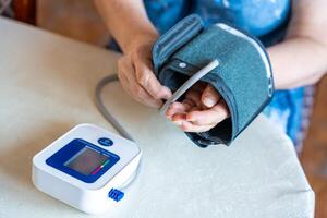 Senior woman finish to check blood pressure level at home, older female suffering from high blood pressure sitting and using a pulsometer, tonometer photo