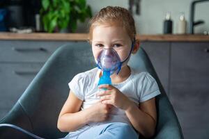 Cute smiling little girl are sitting and holding a nebulizer mask leaning against the face, airway treatment concept. High quality photo