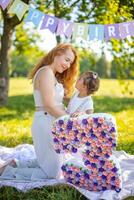 alegre madre y hija teniendo divertido en niño cumpleaños en cobija con papel decoraciones en el parque foto