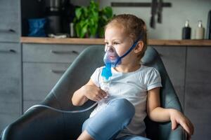 Cute little girl are sitting and holding a nebulizer mask leaning against the face at home on sick leave, airway treatment concept photo