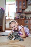 Cute little girl with gray cat lying on carpet in home living room photo