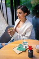 Young business woman holding and drinking coffee in street cafe in city. Portrait of beautiful woman worker waiting client on street of Prague photo