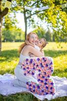 Cheerful mother and daughter having fun on child birthday on blanket with paper decorations in the park photo