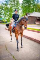 Lovely young woman wearing helmet riding her brown horse photo