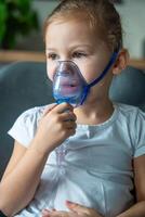 Cute little girl are sitting and holding a nebulizer mask leaning against the face, airway treatment concept. High quality photo