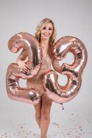 Pretty sexy blonde woman on white background. Portrait of beautiful young lady in beige glitter sequins long evening dress with twenty five shape inflatable balloons in hand. photo