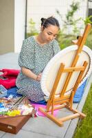 Asian young woman painting picture of lemons on blue blanket in home terrace. High quality photo