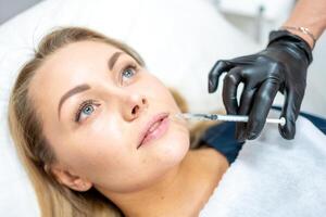 Close-up of woman face and hand in surgical glove holding syringe near her lips, ready to receive beauty treatment. Injection cosmetology, lips augmentation and correction concept. photo