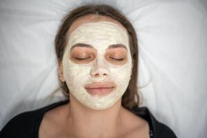 Beautiful happy woman in the spa making face mask treatment. Beauty industry concept. photo