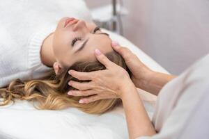 Healer performing by lightly touched access bars therapy on young woman head, stimulating positive change thoughts and emotions. Alternative medicine concept photo