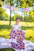 Cheerful girl having fun on child birthday on blanket with paper decorations in the park photo