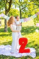 Cheerful mother and daughter having fun on child birthday on blanket with paper decorations in the park photo