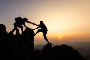 silhouette of Teamwork of two men hiker helping each other on top of mountain climbing team. Teamwork friendship hiking help each other trust assistance silhouette in mountains, sunrise. photo