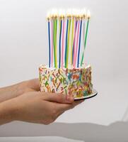 Hands giving birthday cake with many tall candles photo