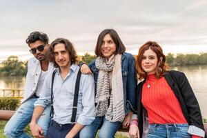 grupo de mejor amigo tener divertido en frente de un grande río en otoño a puesta de sol foto