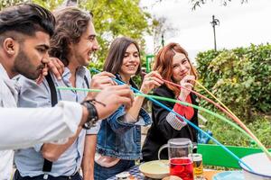 grupo de multicultural amigos teniendo divertido a el jardín fiesta succión cerveza desde vistoso pajitas foto