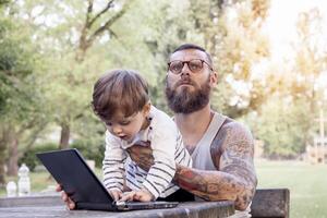 tatuado papá tener divertido con su hijo y ordenador portátil foto