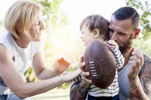 young couple with child having fun at the park with rugby ball photo