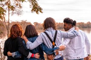 grupo de mejor amigo tener divertido en frente de un grande río en otoño a puesta de sol foto