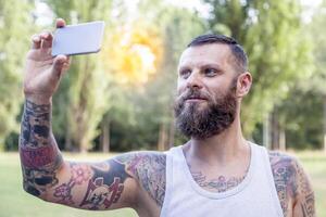 tattooed bearded man takes a selfie in the park photo