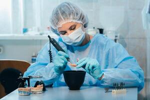 A masked and gloved dental technician works on a prosthetic tooth in his lab photo