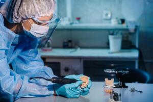 A dental technician in protective clothing is working on a prosthetic tooth in his laboratory photo