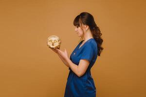 Cute young doctor girl holding a human skull, brown background behind the doctor photo