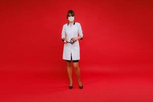 un joven médico en un blanco Saco y médico máscara soportes en un rojo antecedentes foto