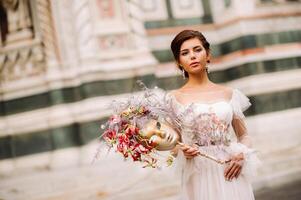 the girl-bride is with beautiful flower pattern as a mask in Florence, stylish bride in a wedding dress standing with a mask in the Old town of Florence. Model girl in Florence photo
