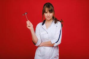 a beautiful doctor girl holds a reflex hammer and smiles at the camera isolated on a Red background photo