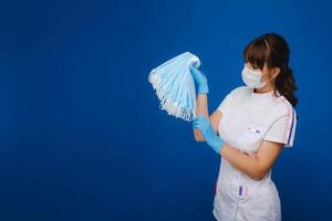 A young girl doctor in a medical mask holds a lot of masks in her hands. A nurse with white masks in her hands on a blue background photo