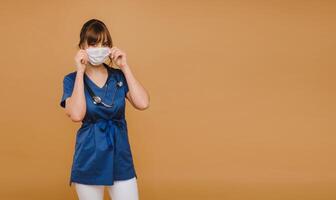 A girl doctor stands in a medical mask, isolated on a brown background photo