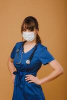 A girl doctor stands in a medical mask, isolated on a brown background photo