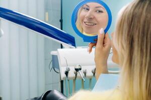 The girl smiles and looks in the mirror in the dentist's office photo