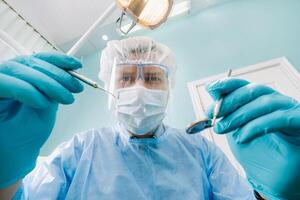 a dentist wearing a protective mask sits nearby and holds instruments in his hands before treating a patient in the dental office photo