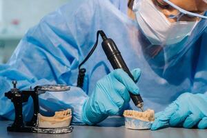 A dental technician in protective clothing is working on a prosthetic tooth in his laboratory photo