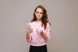 A happy young girl holding a phone looks into it and smiles photo