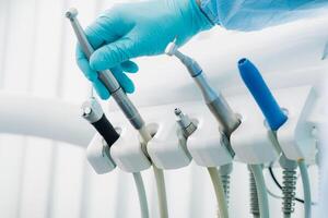 un dentista vistiendo guantes en el dental oficina sostiene un herramienta antes de trabajando foto