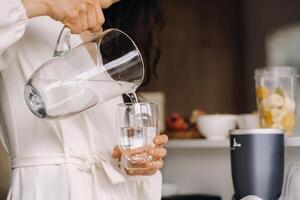 Close-up of the hands of a girl in the kitchen who pours clean water into a glass. Healthy eating photo