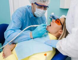 A male dentist with dental tools drills the teeth of a patient with an assistant. The concept of medicine, dentistry and healthcare photo