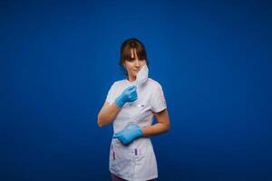A doctor girl stands in a medical mask on an isolated blue background photo