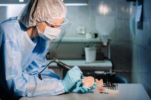 A masked and gloved dental technician works on a prosthetic tooth in his lab photo