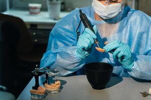 A masked and gloved dental technician works on a prosthetic tooth in his lab photo