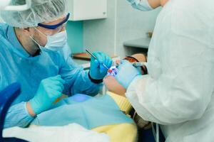 A young beautiful girl in dental glasses treats her teeth at the dentist with ultraviolet light. filling of teeth photo