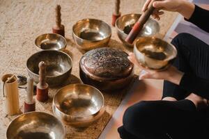 de cerca de un mujer manos sentado en un loto posición utilizando un canto cuenco adentro. relajación y meditación. sonido terapia, alternativa medicamento. tibetano bochas foto